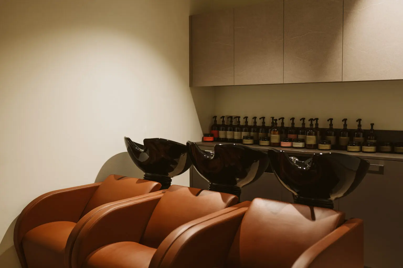 Zona lavatesta con poltrone color cognac e prodotti professionali